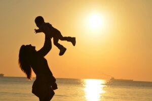 Mother raising her child in the air in front of beach sunset